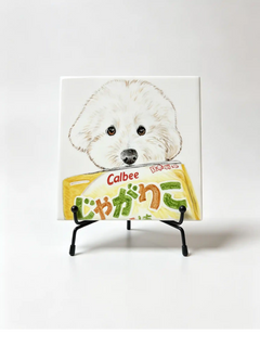 Custom pet portrait tile featuring a white dog holding a Calbee snack bag, displayed on a black metal tabletop easel