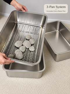 A stainless steel 3-pan pet litter system shown on a beige carpet, with a person's hands holding one pan to demonstrate its design. The set includes a large draining pan with litter pieces visible, a medium pan, and a smaller base pan.